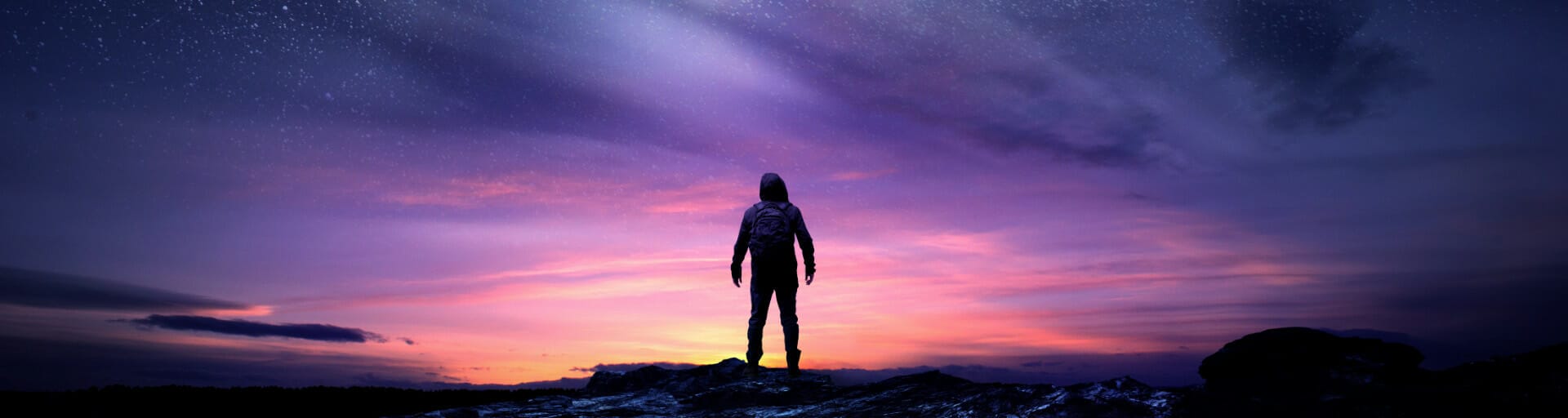 A person stands with their back to the camera facing a vibrant orange and purple night sky with some stars barely visible at the top of the frame.