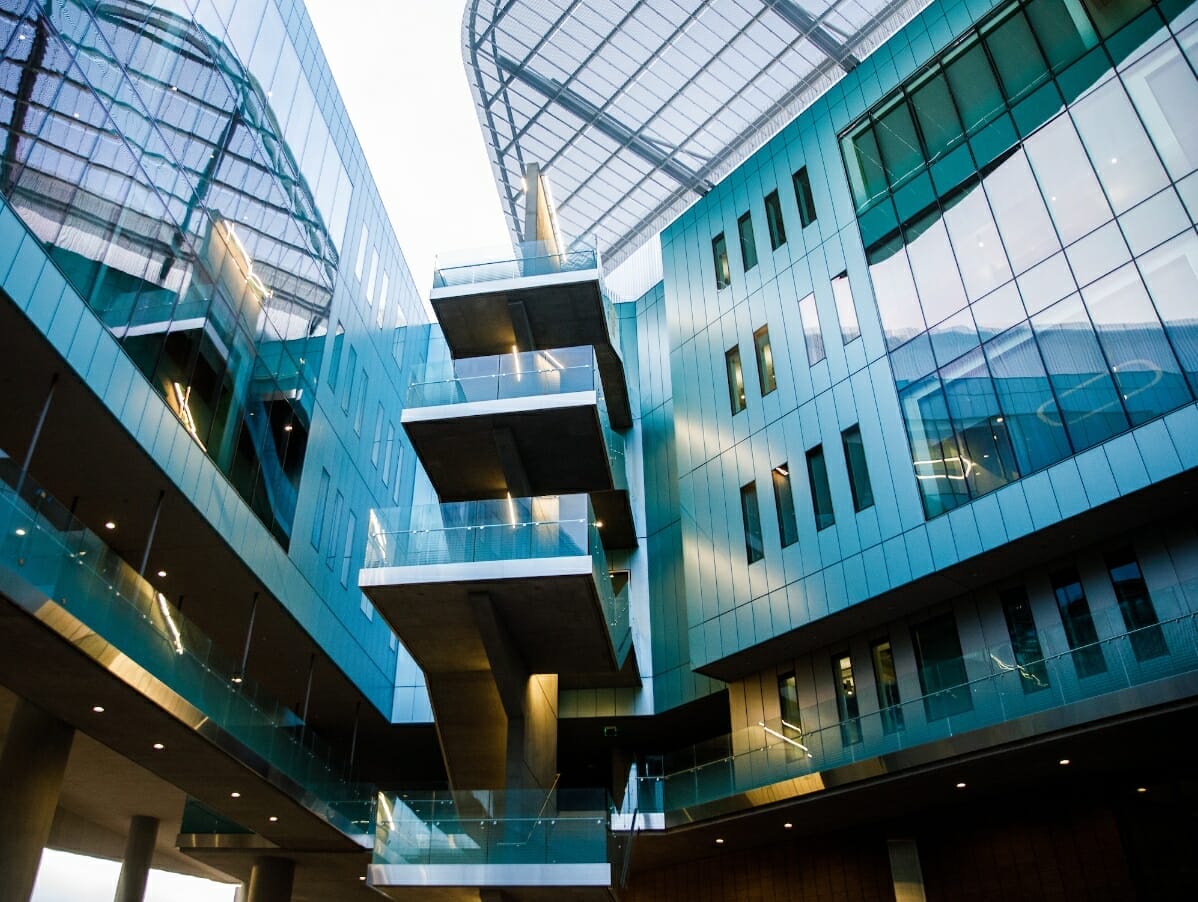 A low-angle image of the Walton Center for Planetary Health, a modern, turquoise building lined with windows and a staircase