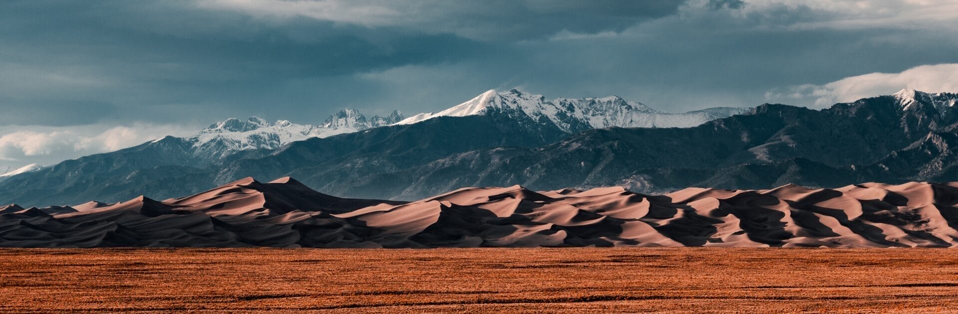 
		Landscape image of a sandy desert with shadowy mountains in the background.		